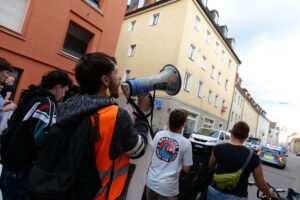 Ein Aktivist mit Warnweste ruft in ein bunt bestickertes Megaphon