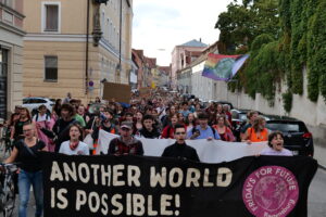 Der Demozug befindet sich in der Ostengasse und macht lautstark auf sich aufmerksam. Auf dem Frontbanner steht "Another World Is Possible!".